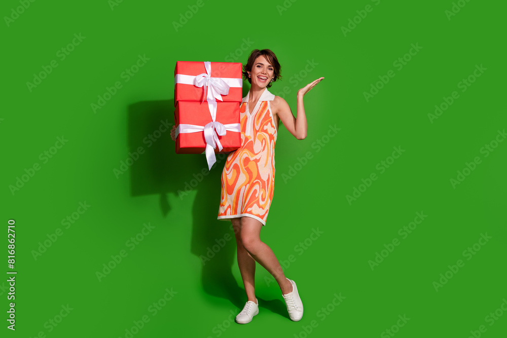 Full body photo of lovely young lady big giftbox hand point empty space dressed stylish colorful garment isolated on green color background Full body photo of lovely young lady big giftbox hand point empty space dressed stylish colorful garment isolated on green color background