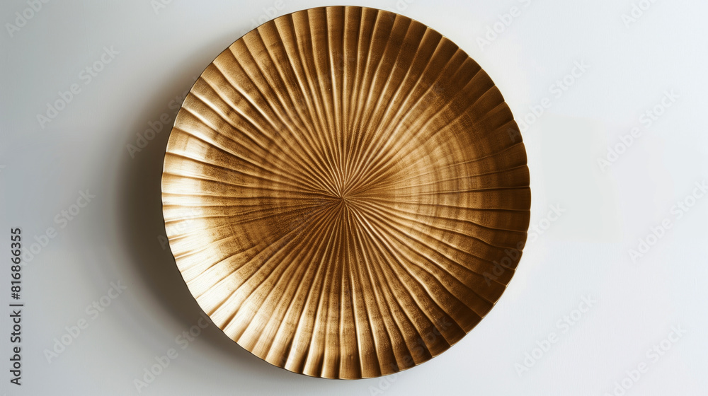 A large, round, golden plate with a textured radial pattern is mounted on a white wall, casting a subtle shadow. The design is elegant and decorative, adding visual interest. A large, round, golden plate with a textured radial pattern is mounted on a white wall, casting a subtle shadow. The design is elegant and decorative, adding visual interest.