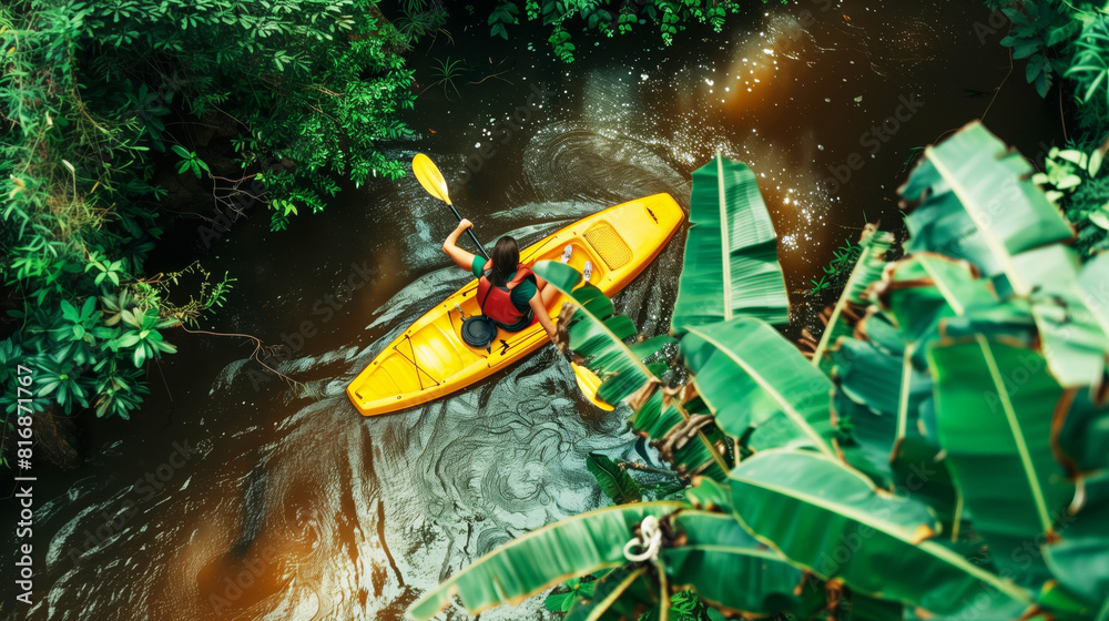 Overhead view of a person paddling a yellow kayak through a narrow, lush, tropical waterway surrounded by dense greenery and banana leaves.