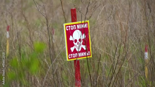 A red warning sign with the inscription booby-trapped with the image of a skull in a field. Humanitarian demining. photo