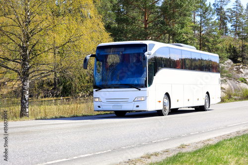 White coach bus transports passengers on road through rural scenery on a day of spring.