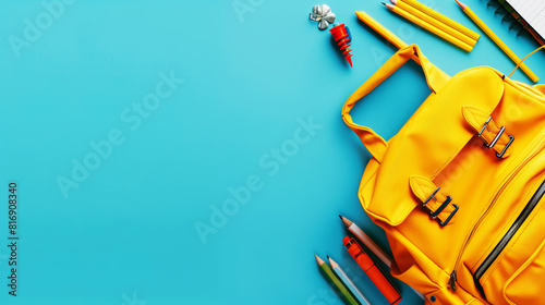 Top view of a yellow backpack with various school supplies including pencils, pens, and a notebook on a blue background. Spacious design allows for text addition. photo