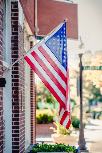 An American flag is hanging from a building on a traditional street in a small town.