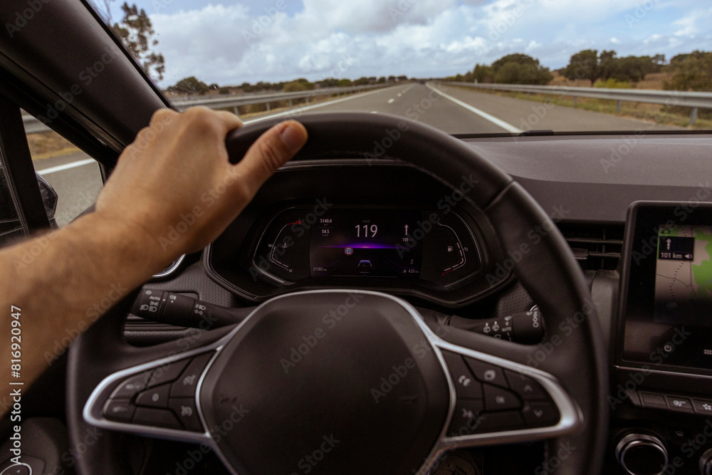 Fototapeta premium Driver view to the speedometer at 119 kmh, on a road blurred. Daylight view from inside a car of driver POV of the road landscape.