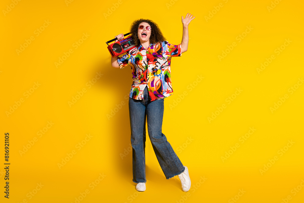 Full size photo of attractive young woman boombox listen music dressed stylish colorful print clothes isolated on yellow color background Full size photo of attractive young woman boombox listen music dressed stylish colorful print clothes isolated on yellow color background