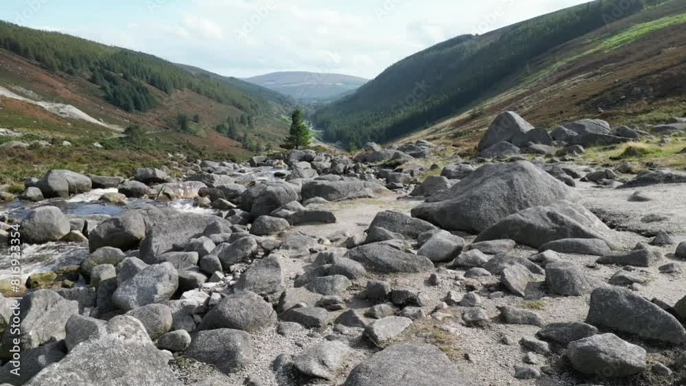 Drone flies over a woman's shoulder as she sits on a rock at the top of the Wicklow Gap, Ireland