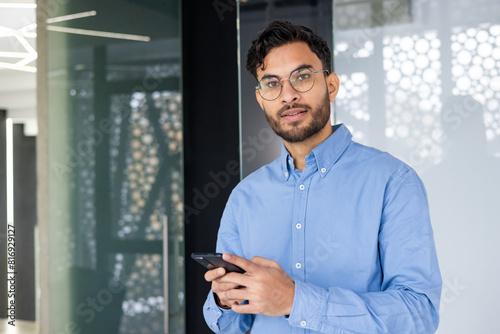 Confident young professional in blue shirt holding smartphone at modern office