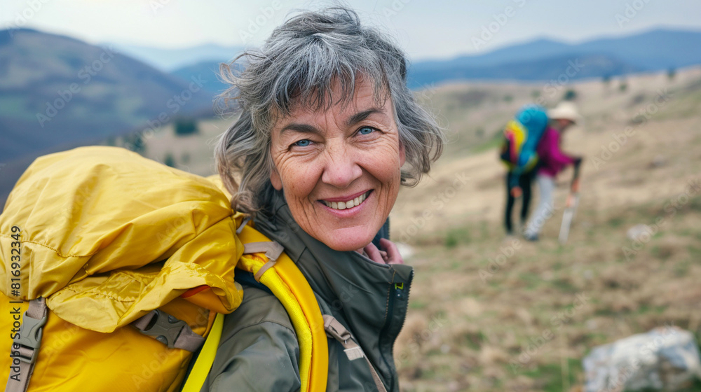 Happy smiling active senior woman with yellow backpack hiking in the mountain with friends. Active healthy lifestyle concept. Happy smiling active senior woman with yellow backpack hiking in the mountain with friends. Active healthy lifestyle concept.