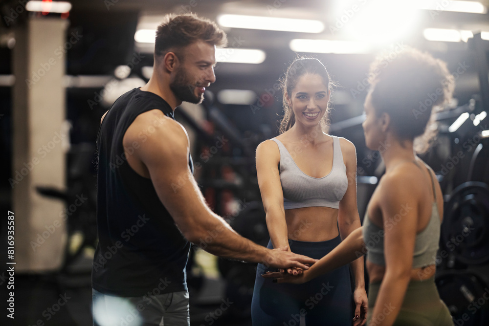 Sportspeople stacking hands in a gym and smiling at each other.