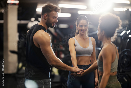 Sportspeople stacking hands in a gym and smiling at each other.