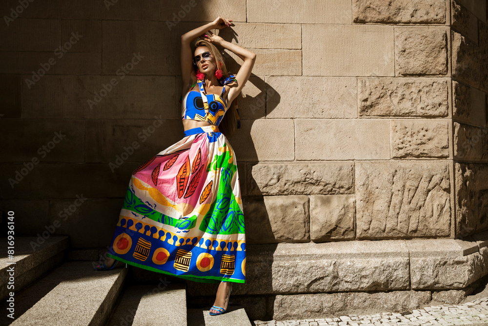Beautiful female model in a colorful summer dress and sexy high heels poses sensually in the city on a sunny summer day. Outdoor session Beautiful female model in a colorful summer dress and sexy high heels poses sensually in the city on a sunny summer day. Outdoor session