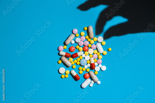 Shadow from hand taking a pill from the heap of pills on blue background.