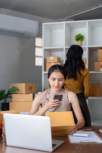 Entrepreneur managing online business from home office. ecommerce owner preparing packages for shipment and checking orders on a smartphone. © Natee Meepian