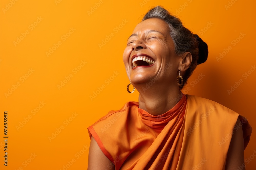 Portrait of a satisfied indian woman in her 50s laughing isolated in soft orange background Portrait of a satisfied indian woman in her 50s laughing isolated in soft orange background