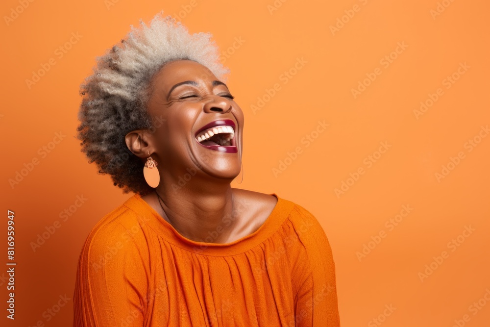 Portrait of a content afro-american woman in her 50s laughing over soft orange background
