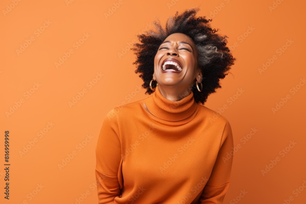 Obraz premium Portrait of a content afro-american woman in her 50s laughing isolated on soft orange background