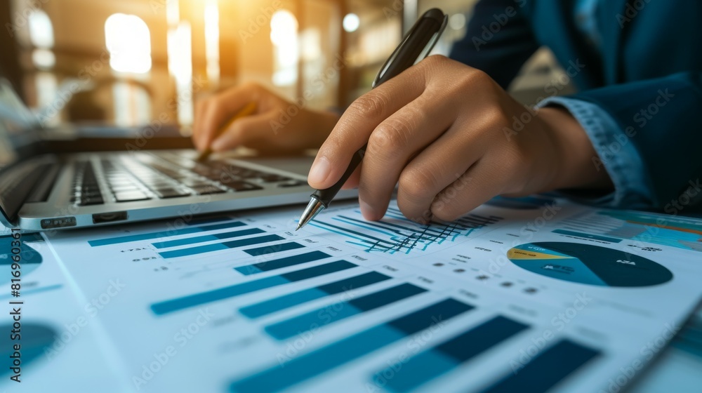 Business man working at the office working. He is working on laptop and has paperwork around him with finance data including graphs and charts Business man working at the office working. He is working on laptop and has paperwork around him with finance data including graphs and charts