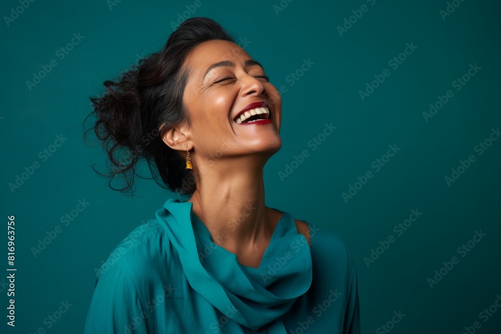 Portrait of a joyful indian woman in her 40s laughing on soft teal background Portrait of a joyful indian woman in her 40s laughing on soft teal background
