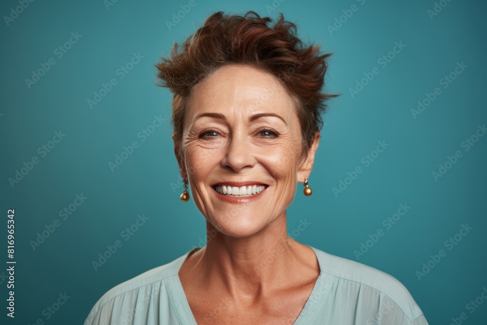 Portrait of a grinning woman in her 50s smiling at the camera on soft teal background