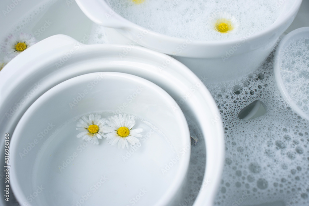 White dishes are filled with water and foam. Close-up of flowers on wet dishes. Place for text. Chamomiles in foam White dishes are filled with water and foam. Close-up of flowers on wet dishes. Place for text. Chamomiles in foam