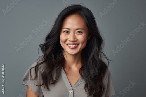 Portrait of a grinning asian woman in her 30s smiling at the camera while standing against soft gray background