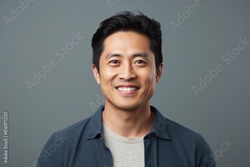 Portrait of a grinning asian man in his 30s smiling at the camera on soft gray background