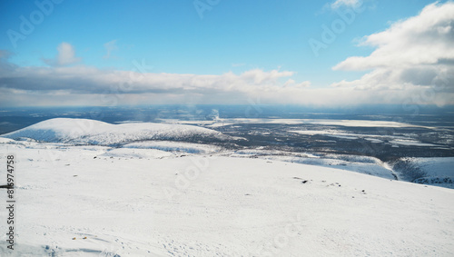 A breathtaking view of snow-covered mountains under a bright blue sky with scattered clouds  showcasing the vast expanse of the winter landscape extending to the horizon.