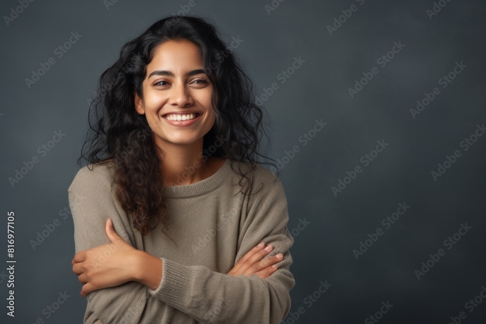 Portrait of a cheerful indian woman in her 20s with arms crossed in front of soft gray background Portrait of a cheerful indian woman in her 20s with arms crossed in front of soft gray background