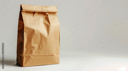A plain brown paper bag with a folded top against a clean, neutral background. The paper bag appears empty and slightly crumpled, suitable for various packaging purposes.
