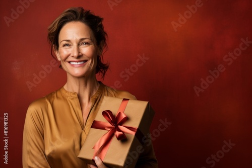 Portrait of a merry woman in her 40s holding a gift isolated on soft brown background © Markus Schröder