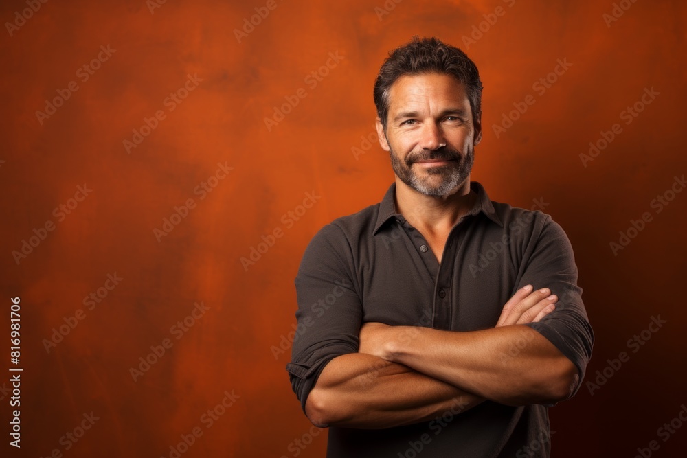 Portrait of a happy man in his 40s with arms crossed isolated in soft brown background