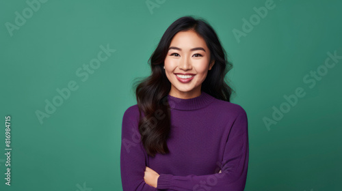 A young woman with long black hair and a purple turtleneck smiling at the camera with her arms crossed. © LightoLife