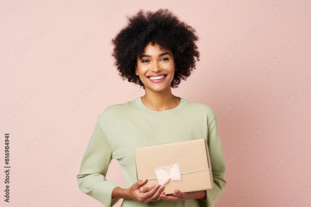 Portrait of a content afro-american woman in her 30s holding a box while standing against pastel or soft colors background Portrait of a content afro-american woman in her 30s holding a box while standing against pastel or soft colors background