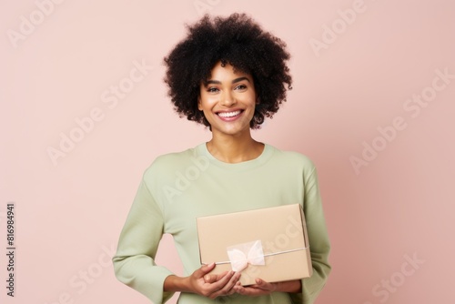 Portrait of a content afro-american woman in her 30s holding a box while standing against pastel or soft colors background