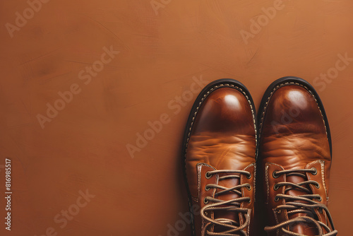 A detailed shot of a pair of stylish leather boots on a solid brown background 