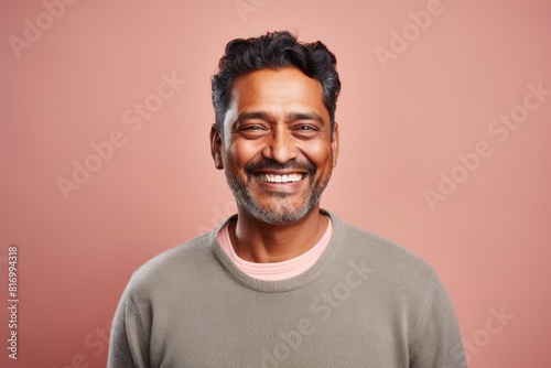 Portrait of a satisfied indian man in his 40s smiling at the camera while standing against pastel or soft colors background