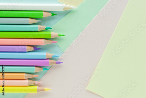 Pastel colored pencils in uneven row on sheets of colored paper