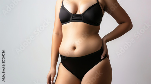 Close-up of a woman wearing a black bikini, focusing on the midsection and part of the upper body, highlighting a natural and confident pose against a neutral background.