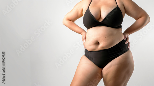 Curvy woman wearing a black bikini, posing confidently against a neutral background. The image emphasizes body positivity and self-confidence.