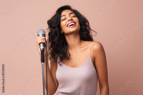 Portrait of a satisfied indian woman in her 20s dancing and singing song in microphone while standing against pastel or soft colors background