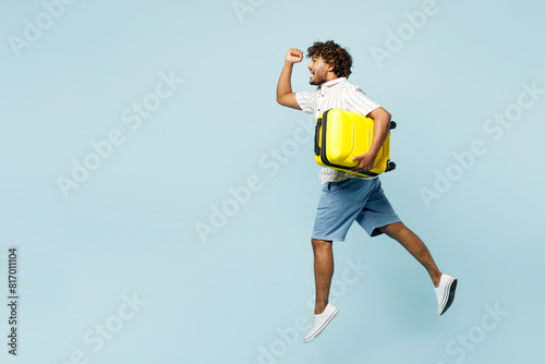 Full body traveler Indian man wear white casual clothes hold suitcase bag run jump isolated on plain blue background. Tourist travel abroad in free spare time rest getaway. Air flight journey concept. #817011104