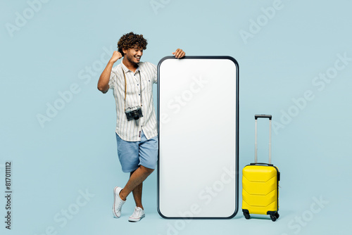 Traveler man wear white casual clothes big blank screen mobile cell phone do winner gesture isolated on plain blue background. Tourist travel abroad in free time rest getaway. Air flight trip concept. #817011112