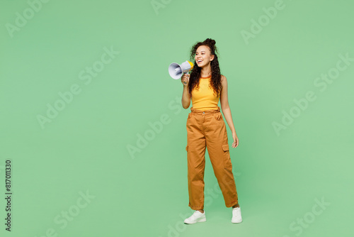 Full body young woman of African American ethnicity wearing yellow tank shirt top hold megaphone scream announces discounts sale Hurry up isolated on plain light green background. Lifestyle concept.