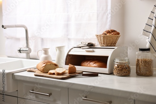 Wooden bread basket with freshly baked loaves on white marble table in kitchen photo