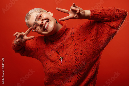 A beautiful short-haired blonde wearing glasses and an orange sweater poses in the studio against an orange background. Emotions! Grain effect used