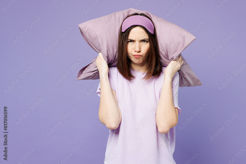 Young sad mad woman wearing pyjamas jam sleep eye mask rest at home hold pillow cover ears from neighbours noise snoring isolated on plain pastel light purple background. Bad mood night nap concept. Young sad mad woman wearing pyjamas jam sleep eye mask rest at home hold pillow cover ears from neighbours noise snoring isolated on plain pastel light purple background. Bad mood night nap concept.