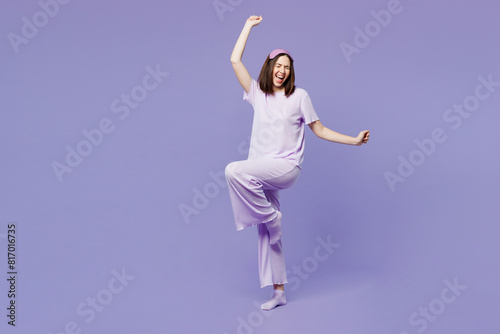 Full body young woman wear pyjamas jam sleep eye mask rest relax at home hold pillow do winner gesture clench fists raise up leg dance isolated on plain purple background. Good mood night nap concept. © ViDi Studio