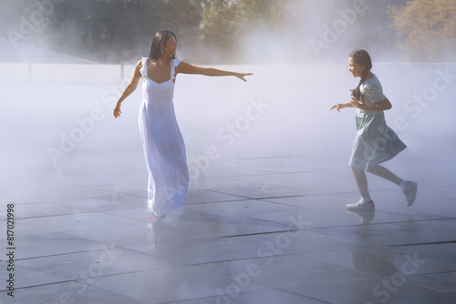 Woman her daughter having fun in the urban vapor fountain photo