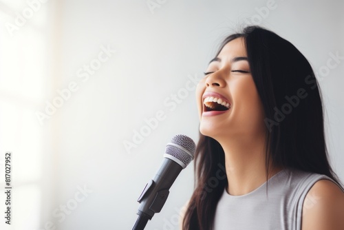 Portrait of a happy asian woman in her 40s dancing and singing song in microphone isolated on minimalist or empty room background