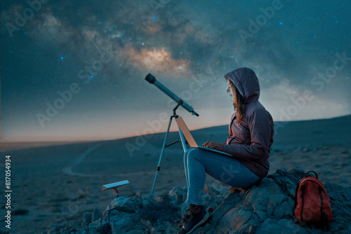 digital nomad woman sitting with a laptop in the desert at night next to a telescope with milky way at night